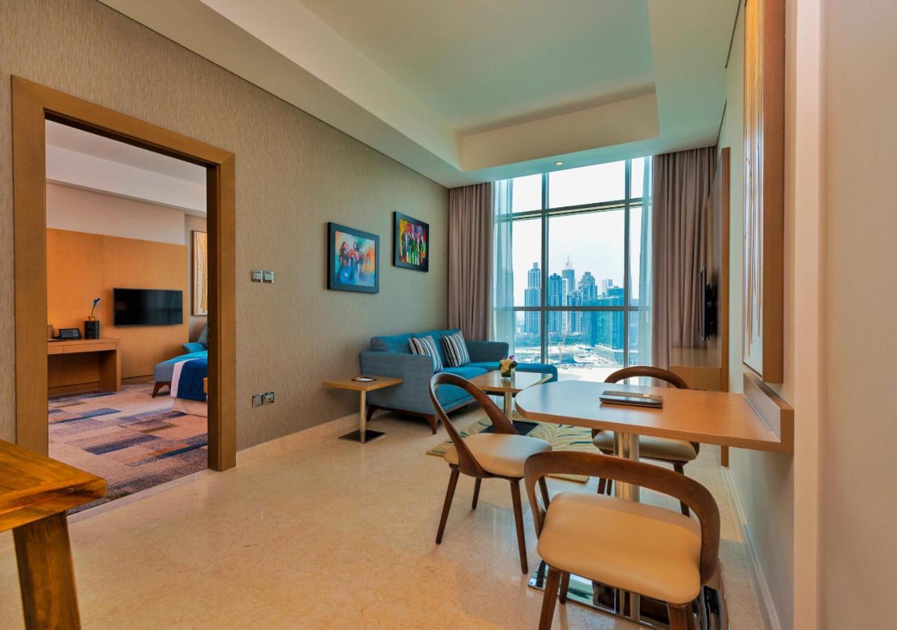 Canal Central Hotel Business Bay Dubai Exterior foto The photo shows a modern interior space, likely a living area or suite. On one side, there’s a small dining table with chairs, and on the other, a comfortable couch positioned near large windows that allow natural light to fill the room. The walls ar