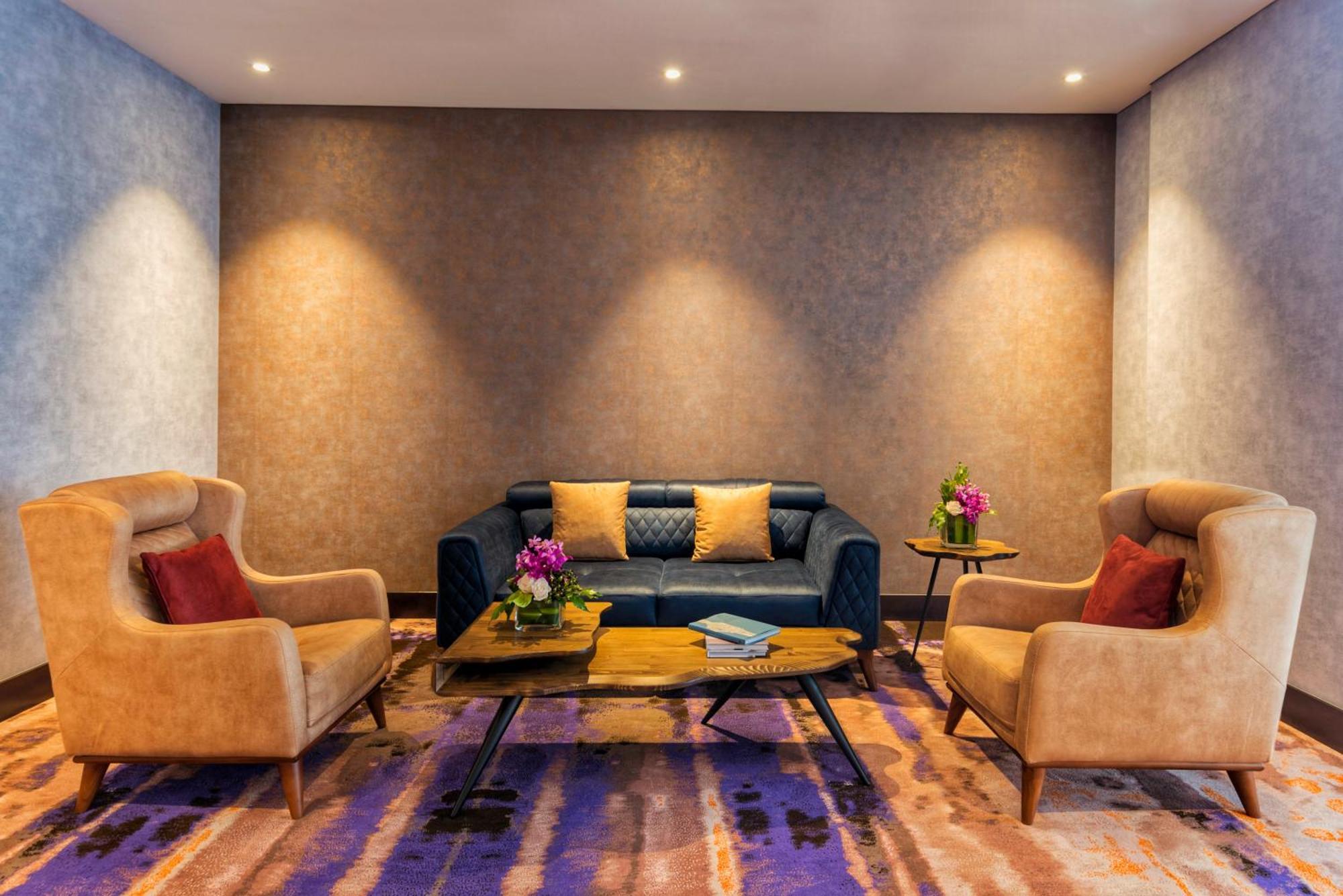Canal Central Hotel Business Bay Dubai Exterior foto The photo shows a cozy and stylish seating area. There is a dark blue sofa in the center, accented with colorful cushions. On either side of the sofa, there are two beige armchairs, each with red cushions. A wooden coffee table sits in front of the s