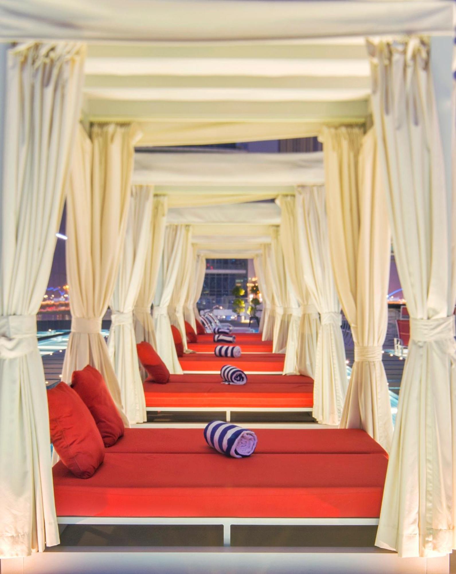 Canal Central Hotel Business Bay Dubai Exterior foto The photo shows a series of elegant lounging areas, likely in a luxurious outdoor setting. Each area is framed by white curtains, creating a cozy, intimate atmosphere. The lounging beds are cushioned with red fabric and feature rolled towels for rela